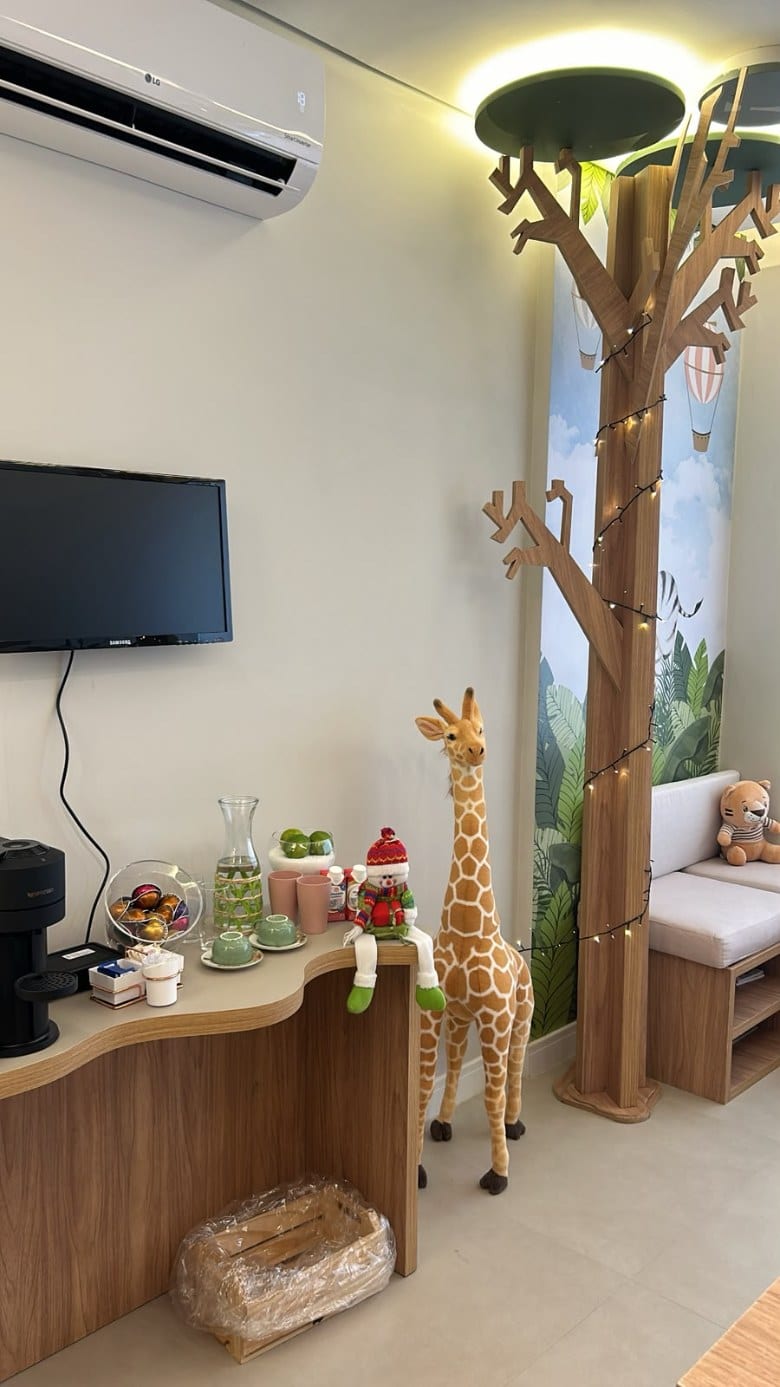 Estação de café e TV na sala de espera, com girafa de pelúcia